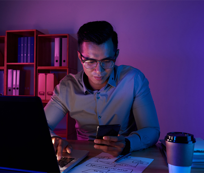 employee checking phone while working on laptop